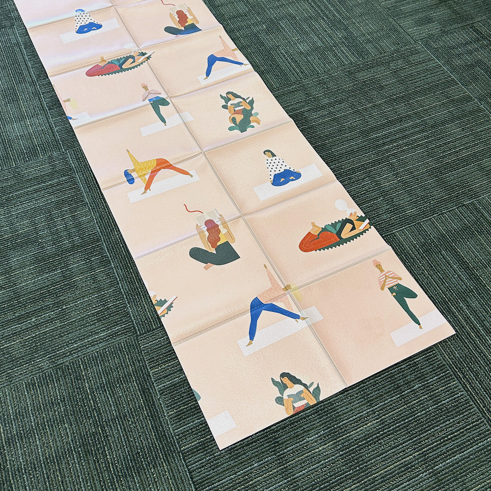 an unfolded pale pink yoga mat with cartoon images of women reading or doing yoga poses