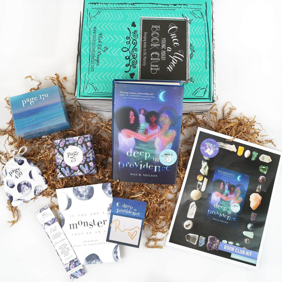 A hardcover edition of Deep in Providence leans against a green Once Upon a Book Club box. In front of the book are a blue square box, blue and purple square box, white drawstring bag, bookmark, quote card, signature card, and bookclub kit. The boxes and bags all have page numbers on them.
