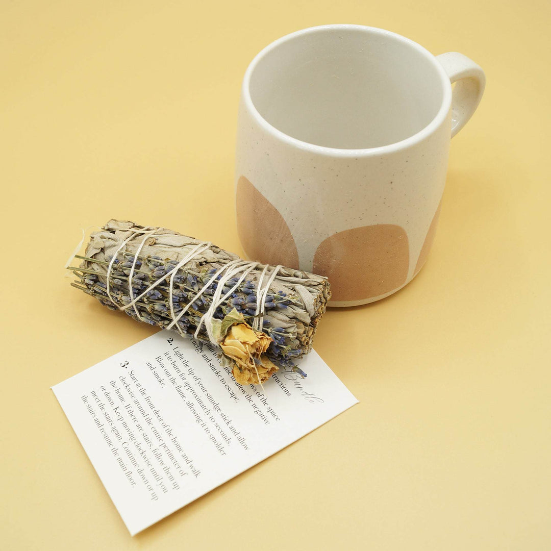 a white speckled mug stands next to a bundle of sage