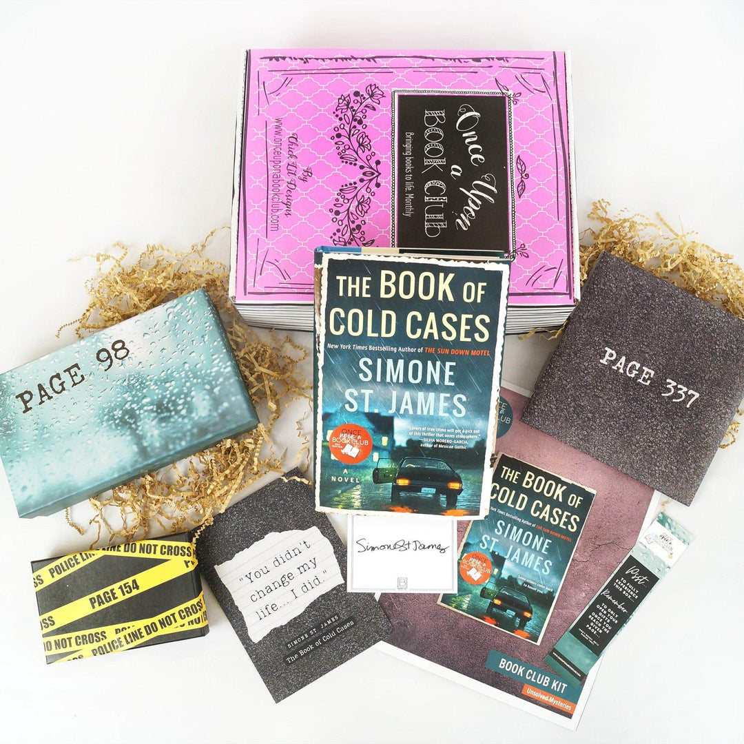 A hardcover edition of The Book of Cold Cases in front of a pink Once Upon a Book Club box. In front of the box are a light blue box, black and yellow box, quote card, signature card, bookclub kit, bookmark, and black envelope. The boxes and envelope all have page numbers on them