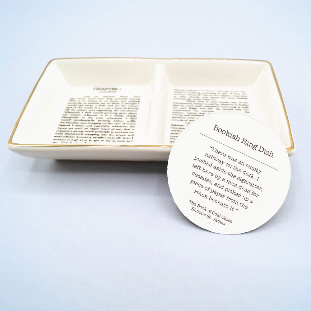 Ceramic ring dish with printed book text and circular card describing its "Bookish Ring Dish" theme.
