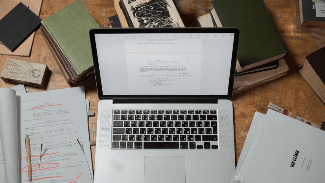 Laptop open with a screenplay on screen, surrounded by books, notes, and glasses, ready for a cozy writing session.