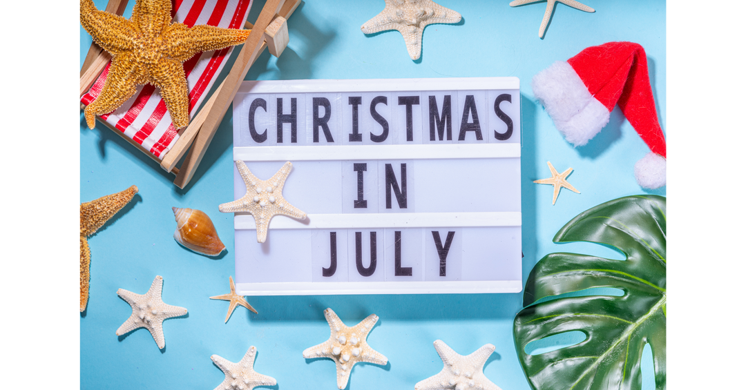 Christmas in July sign surrounded by seashells, starfish, tropical leaves and a Santa hat, blending festive cheer with summer vibes.
