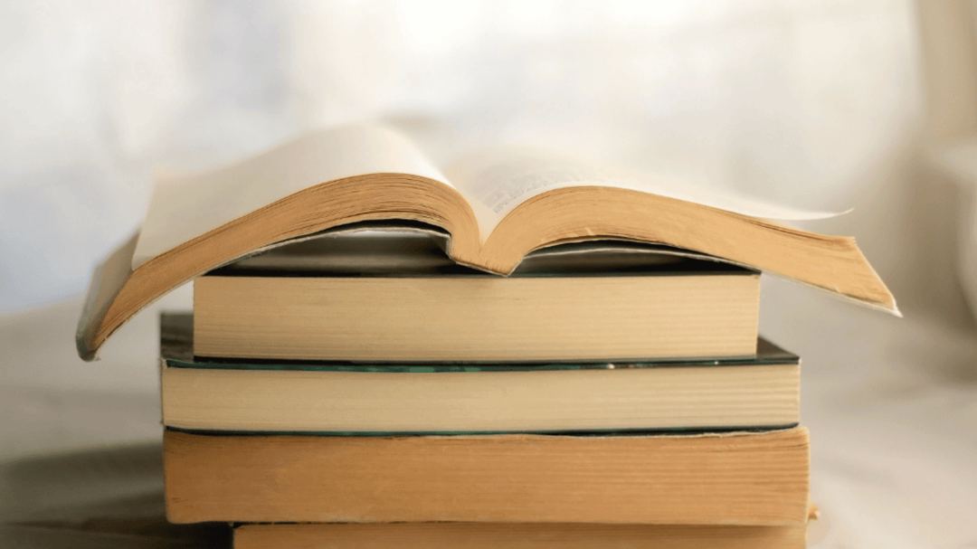 A stack of hardcover books with one open book resting on top, pages gently curved.