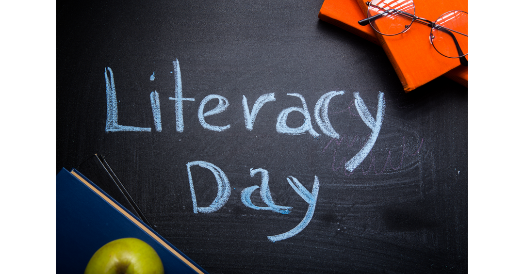 Chalkboard with the words “Literacy Day” surrounded by school supplies and an apple.