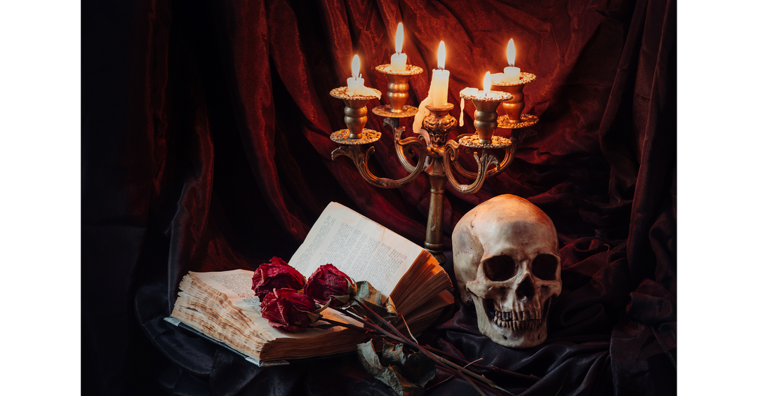 Gothic autumn reading display with an open book, red roses, skull, and lit candelabra against dark burgundy fabric.