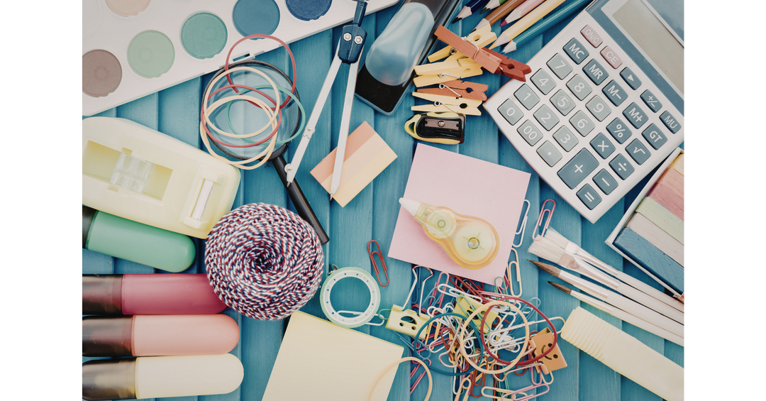 Flat lay of colorful crafting supplies, including scissors, paper clips, paint palette, calculator, and stationery on a blue background.