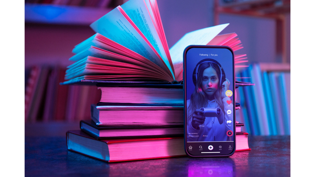 A stack of books with a smartphone propped up in front, displaying a woman in headphones on a social media app, illuminated by neon lighting.