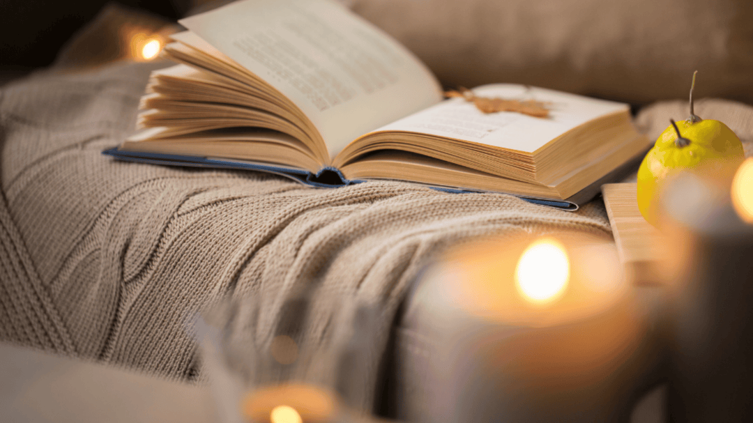 An open book rests on a cozy knitted blanket surrounded by candlelight and soft autumn vibes.