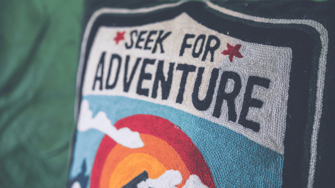 Embroidered pillow patch reads "Seek for Adventure" with a colorful sunset and mountain design.