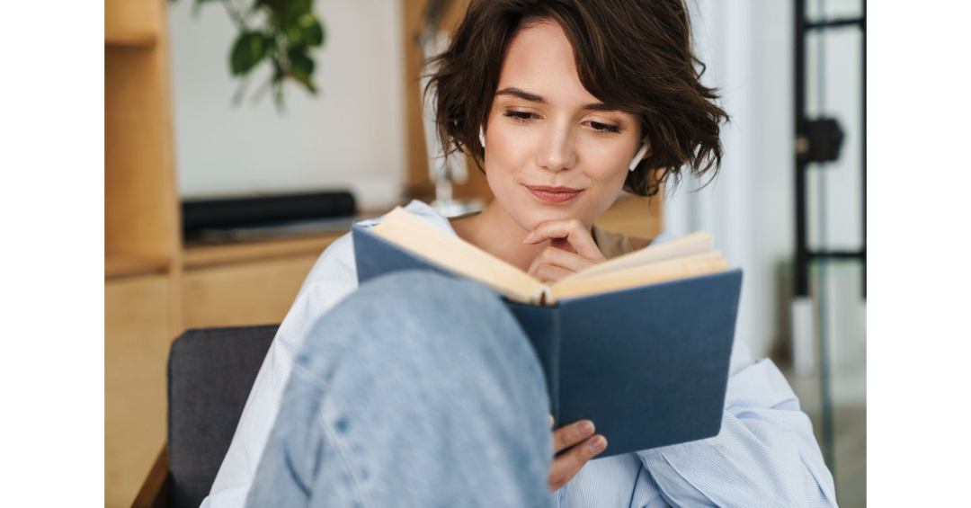 Woman with short brown hair wearing wireless earbuds, thoughtfully reading a book.
