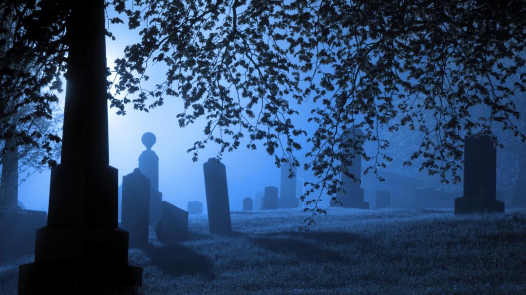A misty graveyard at night, with silhouettes of tombstones under a tree's branches, lit in a moody blue.