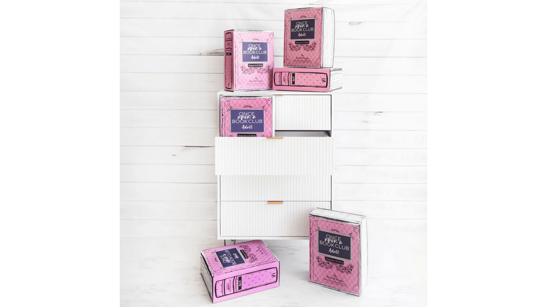 Stacked pink Once Upon a Book Club boxes styled to look like books on and around a modern white dresser.
