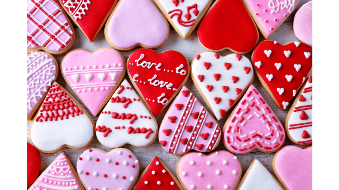 Assorted heart-shaped Valentine’s cookies decorated in red, pink and white icing, arranged closely together on a wooden surface.