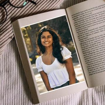 An open book with text on the right side and a picture of the Indian American young adult author Ananya Devarajan on the left.