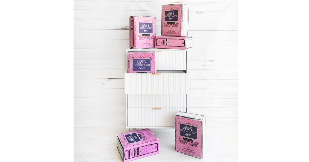 Stacked pink Once Upon a Book Club boxes styled to look like books on and around a modern white dresser.