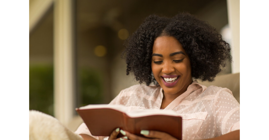 Woman smiling while reading a book in a cozy setting, capturing the joy of getting lost in a great story.