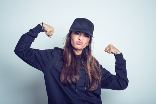 Confident woman flexing muscles, wearing a cap and making a funny face.