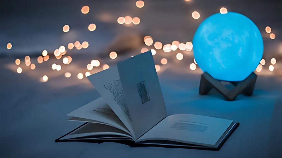 An open book with illustrated pages placed on a blue surface, next to a glowing blue orb, with string lights in the background.