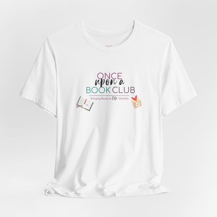 A digital rendering of a white graphic T-shirt hanging on a clean white background. The shirt features the text 'Once Upon a Book Club' in pink, teal, and dark purple lettering, with smaller text reading 'bringing books to life, monthly.