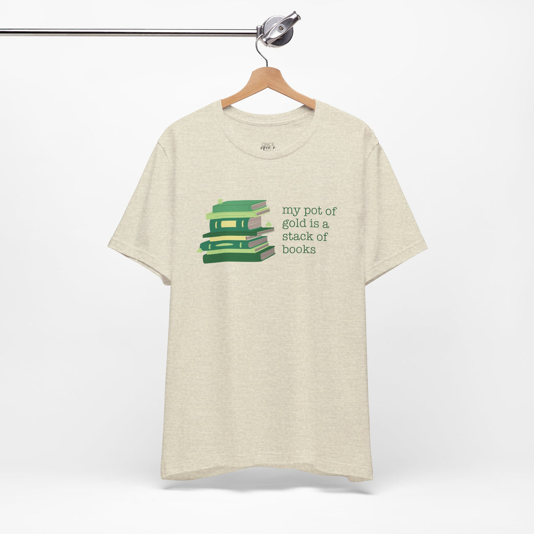 Beige t-shirt with green stack of books and clovers graphic and text "my pot of gold is a stack of books" on a white background