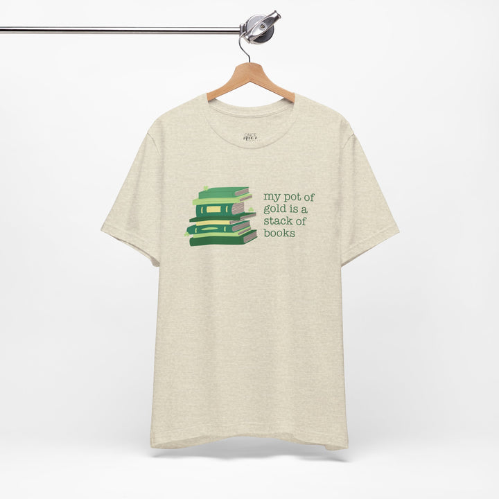 Beige t-shirt with green stack of books and clovers graphic and text "my pot of gold is a stack of books" on a white background