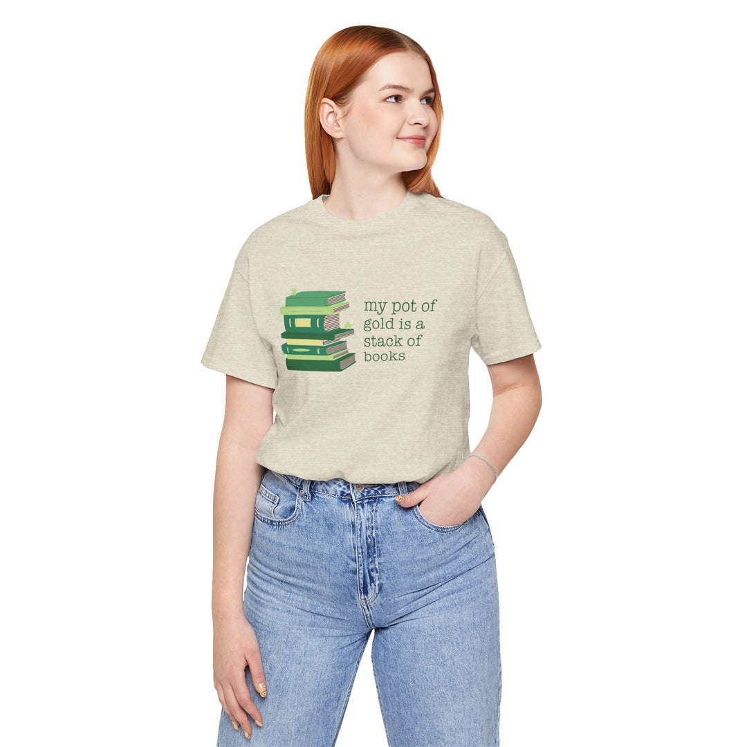 Person wearing a beige t-shirt with green stack of books and clovers graphic and text "my pot of gold is a stack of books"  standing against a white background
