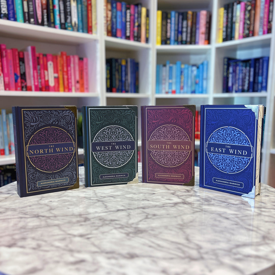 Four books titled 'North Wind', 'West Wind', 'South Wind', and 'East Wind' on a marble surface with a bookshelf in the background.