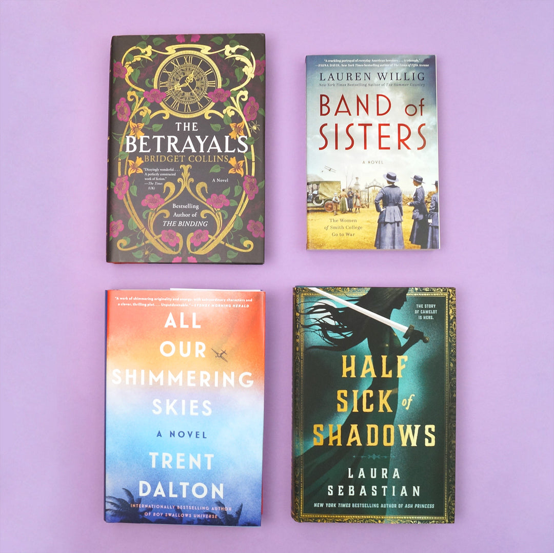 a hardcover copy of The Betrayals by Bridget Collins, All Our Shimmering Skies by Trent Dalton, and Half Sick of Shadows by Laura Sebastian. A paperback copy of Band of Sisters by Lauren Willig. All four books sit on a purple background.