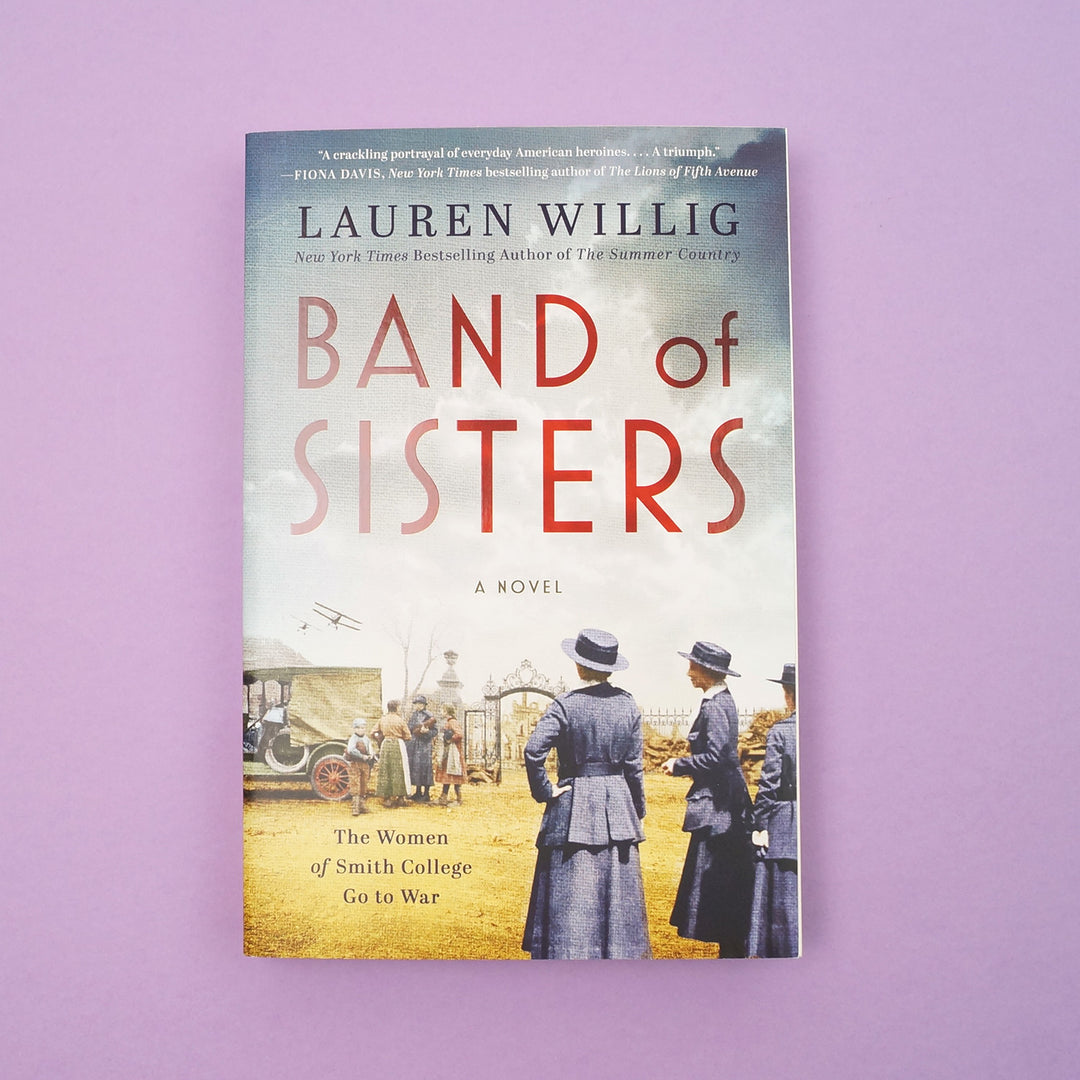 A paperback edition of "Band of Sisters" by Lauren Willig sits on a purple background.