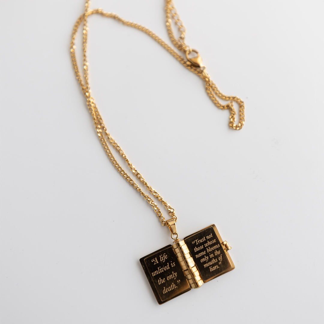 A gold necklace with an open book. The book's pages are also gold and each page has a different quote engraved on it.