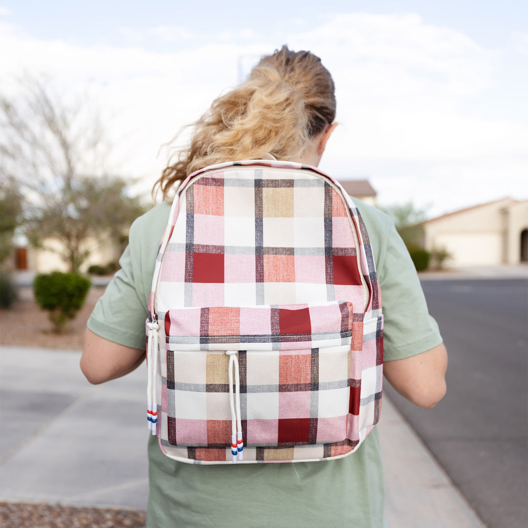 Person wearing a pink plaid backpack outdoors on a sidewalk