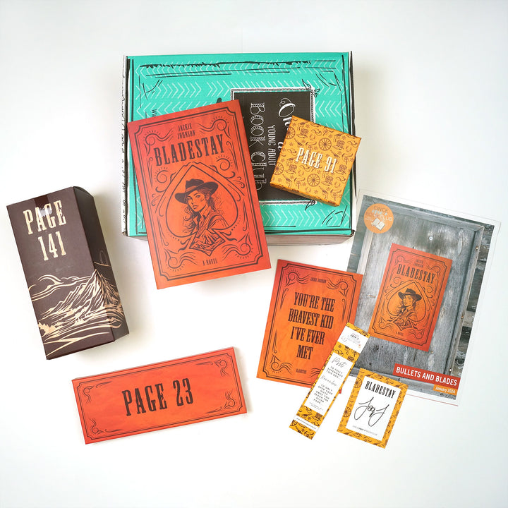 A green box lays on a white background. On top of the box is a hardcover, exclusive edition of BLADESTAY by Jackie Johnson featuring an orange cover with black detailing including a girl in a cowboy hat. Surrounding this are three gift boxes wrapped in various, western-themed packaging labeled with page numbers meant to only be opened when you reach the designated page number. Also pictured is a quote print, bookmark, signed book plate from the author, and a Book Club Kit with information about the box.