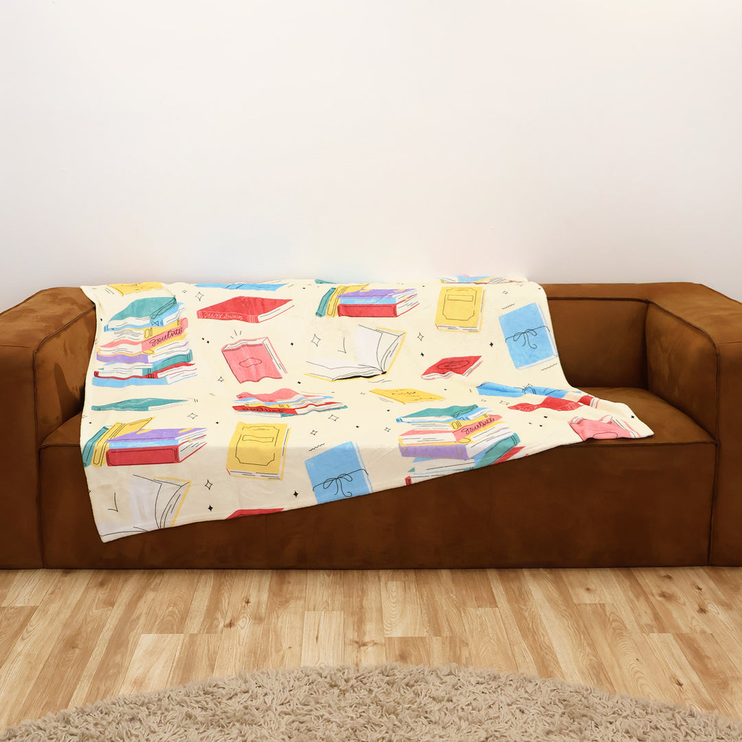 Colorful butter yellow book-patterned blanket on a brown couch against a white wall.