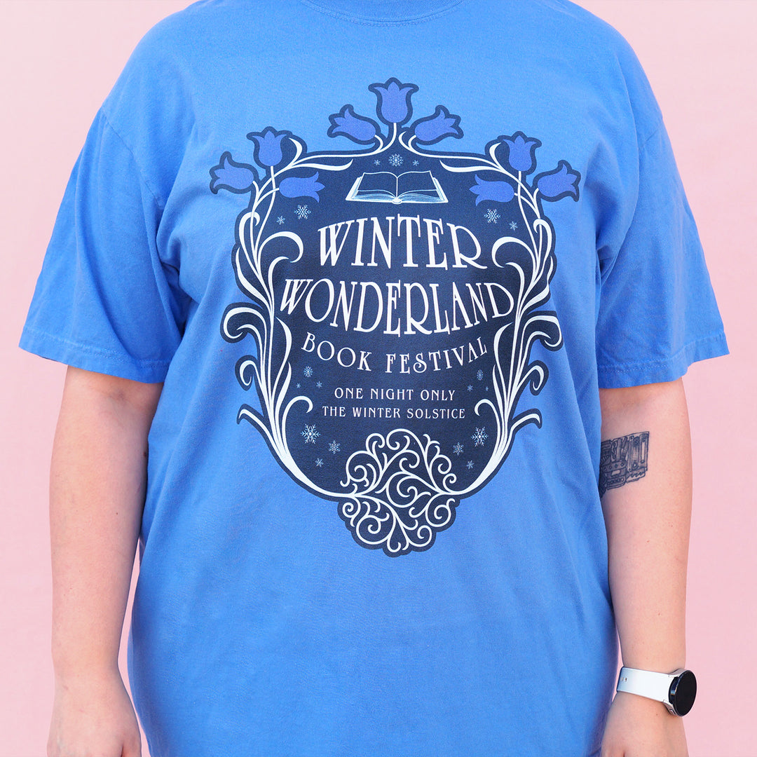 Blue t-shirt with 'Winter Wonderland Book Festival' design on a pink background