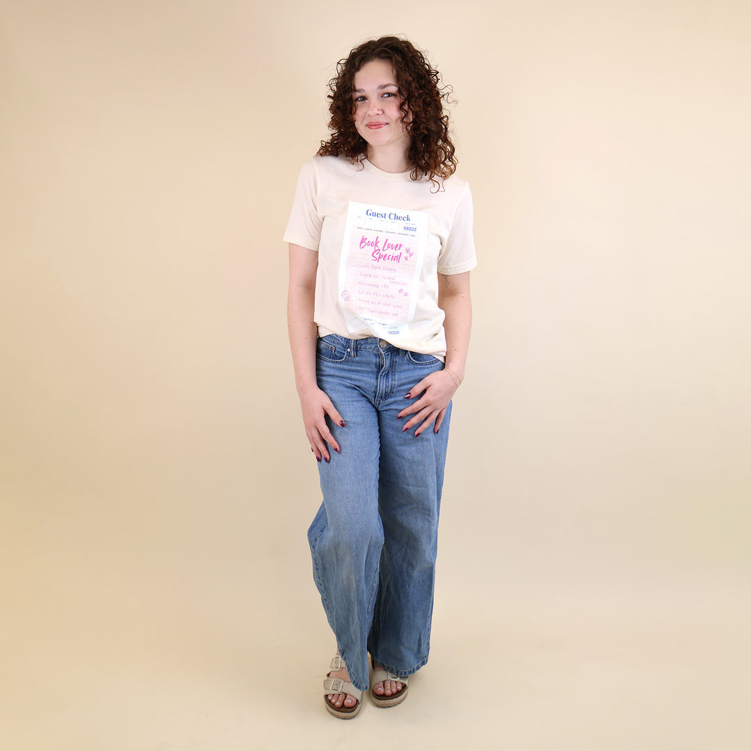 Woman wearing a cream t-shirt with a printed 'Book Lover Special' Guest Check design and jeans on a beige background