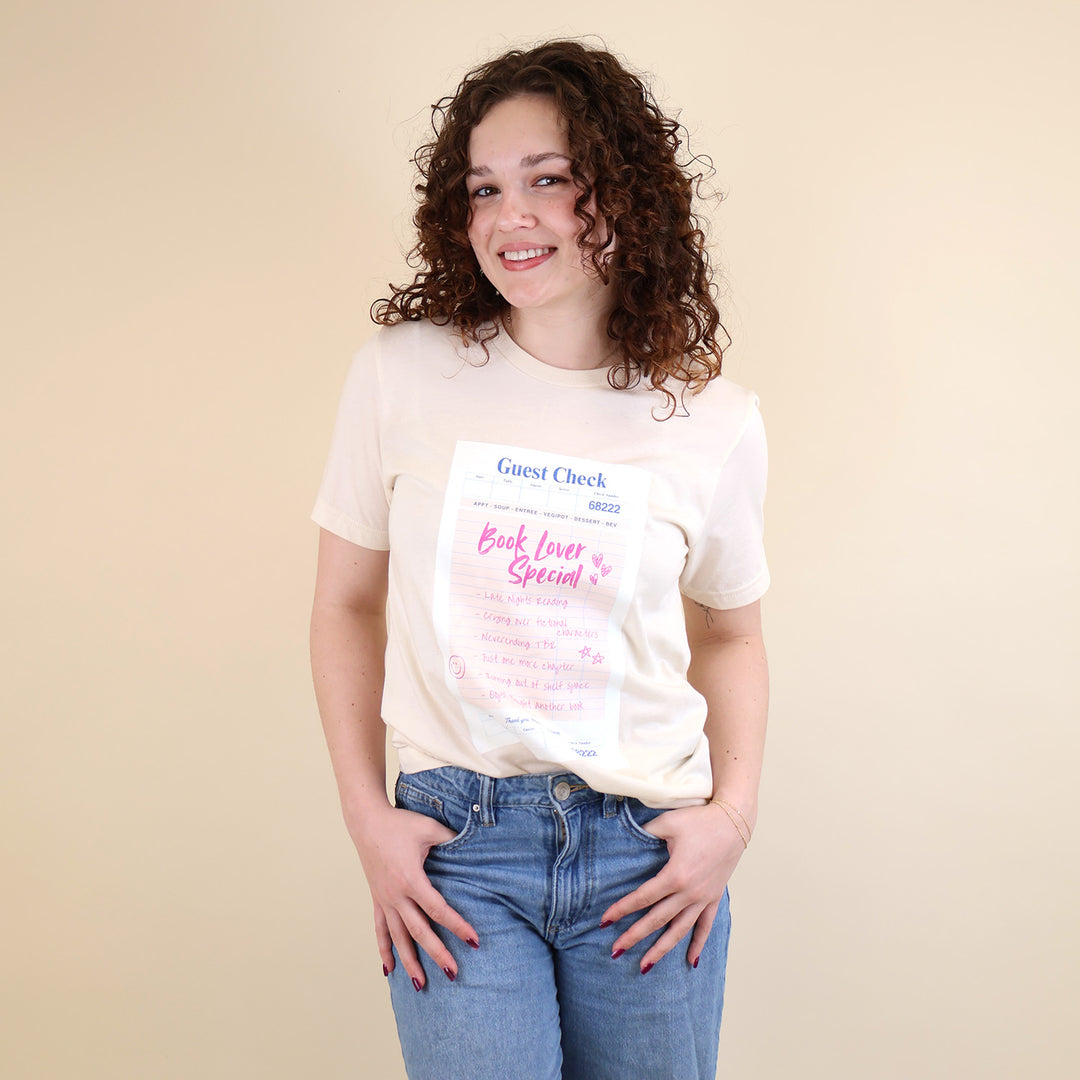 Woman wearing a cream t-shirt with a printed 'Book Lover Special' Guest Check design on a beige background