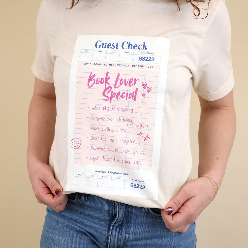 Woman wearing a cream t-shirt with a printed 'Book Lover Special' Guest Check design on a beige background