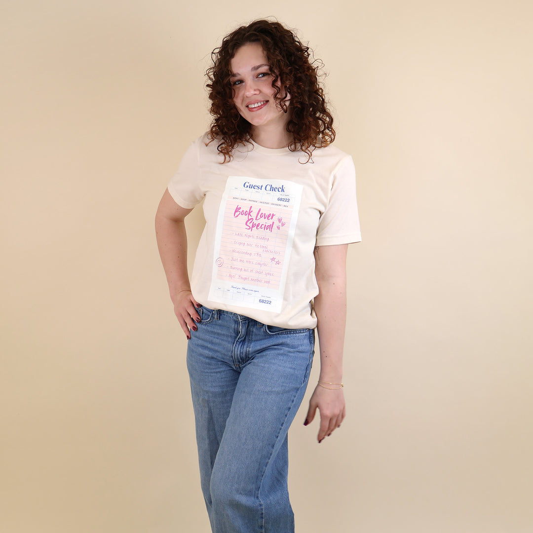 Woman wearing a cream t-shirt with a printed 'Book Lover Special' Guest Check design on a beige background