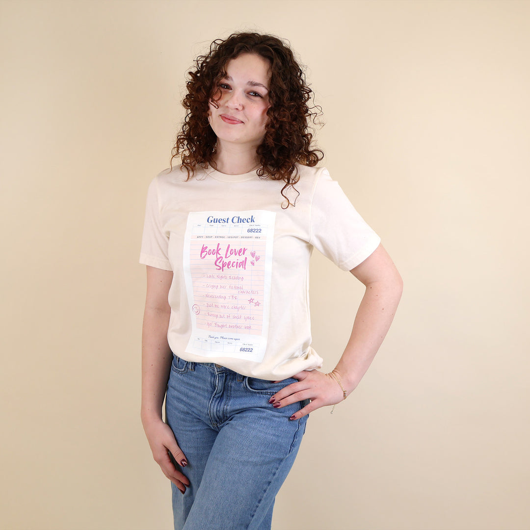 Woman wearing a cream t-shirt with a printed 'Book Lover Special' Guest Check design on a beige background