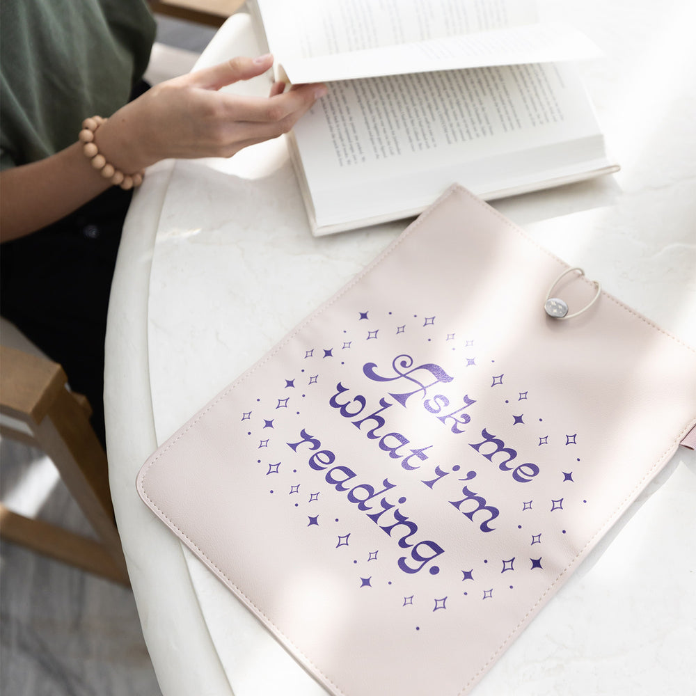 The "What I'm Reading" booksleeve sits on a table next to a person turning a page in a book.