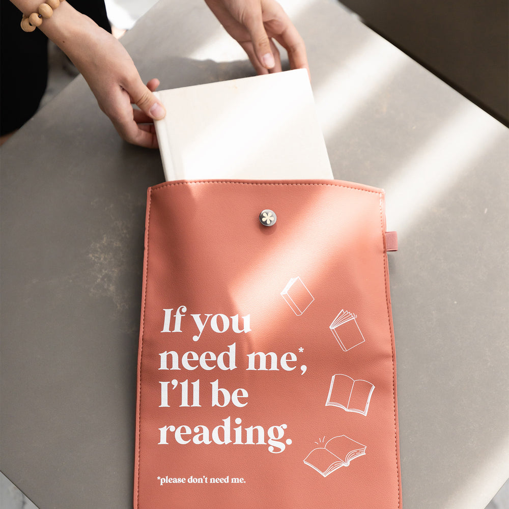 The "Don't Need Me" booksleeve lays on a table while a pair of hands pull a book from within it.