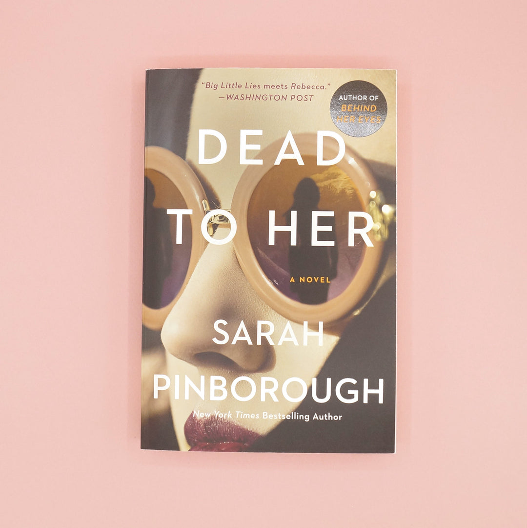 A paperback copy of Dead to Her by Sarah Pinborough on a pink background.