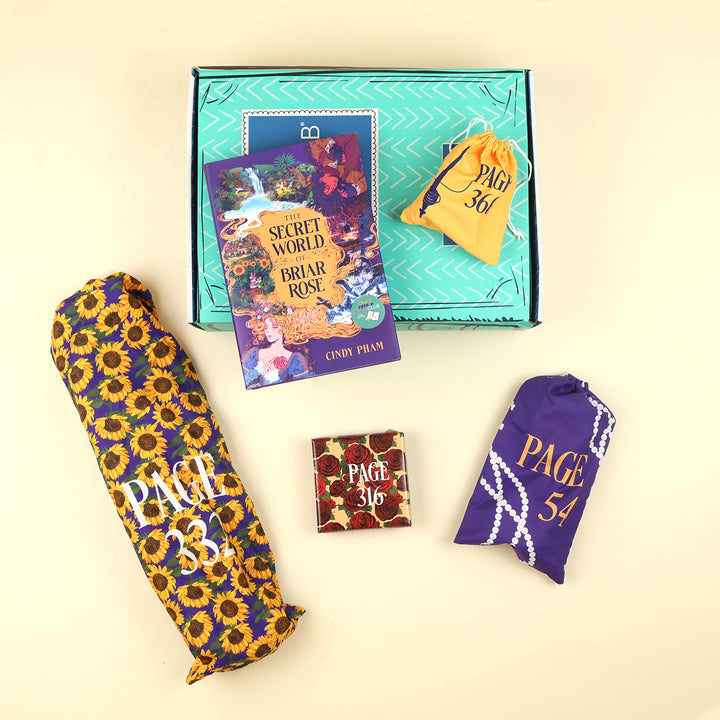 A new deluxe hardcover copy of The Secret World of Briar Rose by Cindy Pham sits on a green OUABC box. Also pictured are four wrapped gifts labeled with page numbers to open as you read!