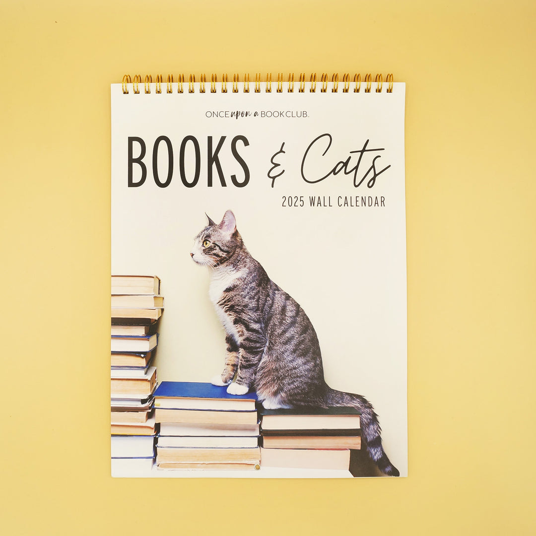 A 2025 Wall Calendar of Books & Cats. showing a gray cat on the front standing on three stacks of books
