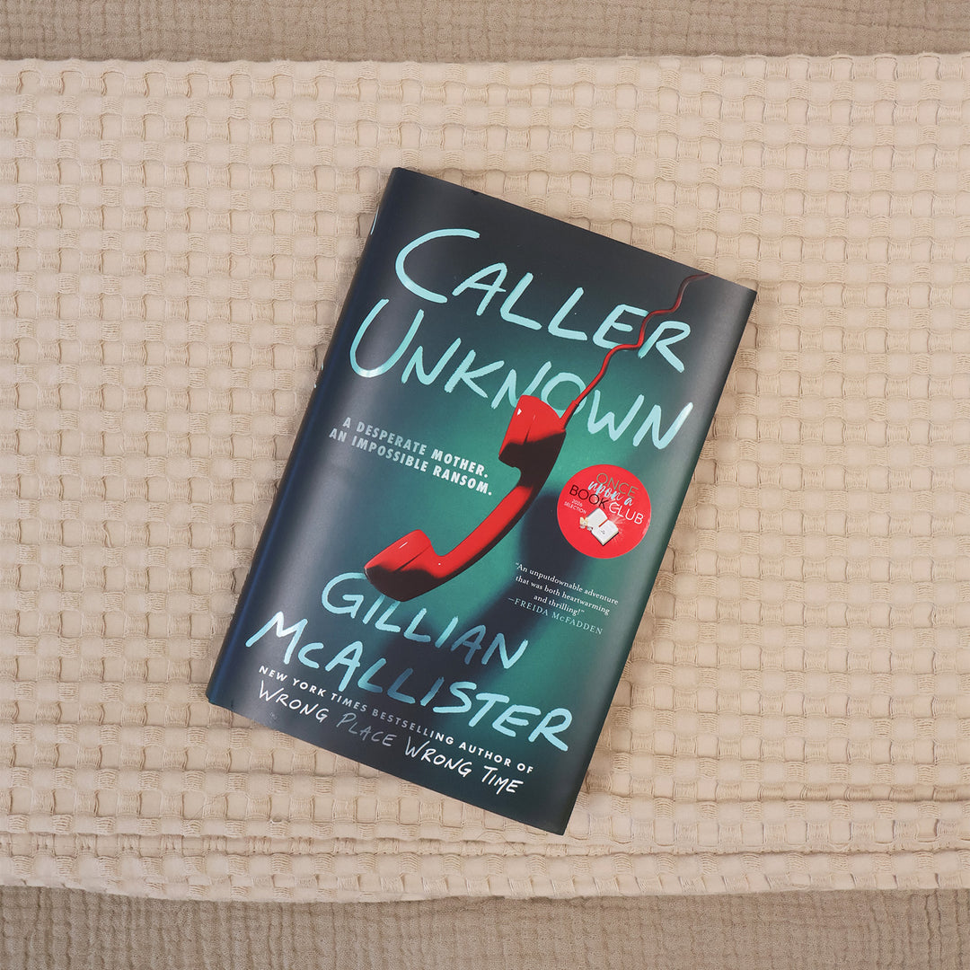 A book titled "Caller Unknown" by Gillian McAllister lies diagonally on a textured beige woven blanket. The book cover is dark teal with light blue lettering and a prominent red telephone receiver graphic.
