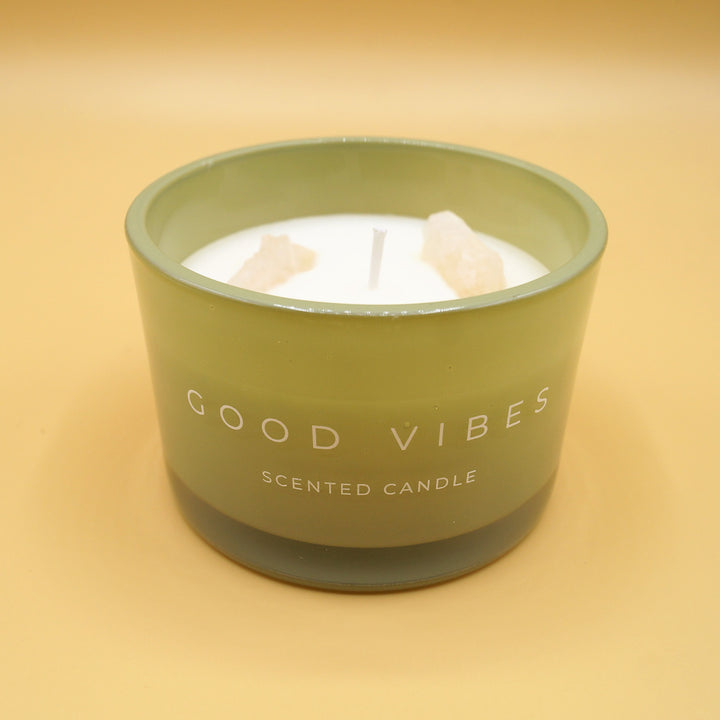 a green candle with white wax and crystals in it labeled "Good Vibes scented candle" on a yellow background
