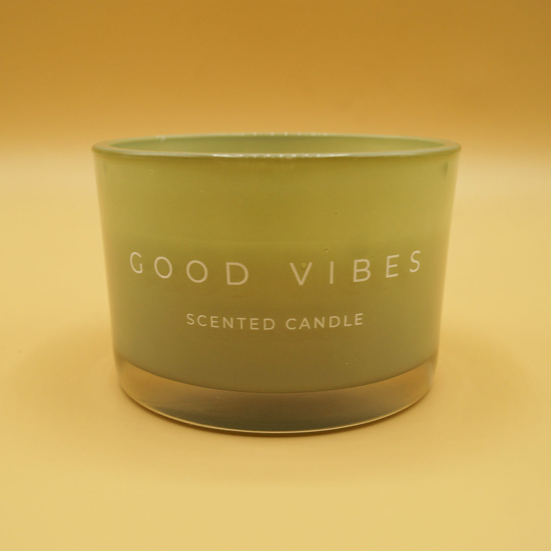 a green candle labeled "Good Vibes scented candle" on a yellow background