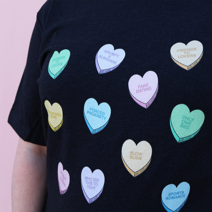 Black t-shirt with colorful heart-shaped trope designs on a pink background