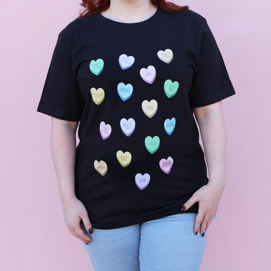 Person wearing a black t-shirt with colorful heart-shaped letters against a pink background